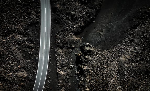 A modern asphalt road running through picturesque volcanic fields with black fossilized lava, aerial view from a drone of the highway between lava formations.