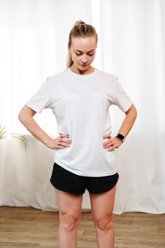 A woman stretches her neck and shoulders in a bright room surrounded by indoor plants during a home workout