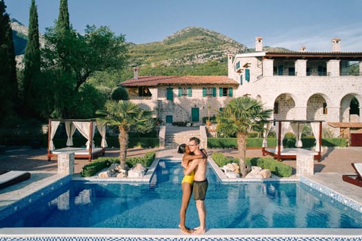 Woman kisses man cheek while hugging him on the edge of a swimming pool in the courtyard of an ancient villa. High quality photo
