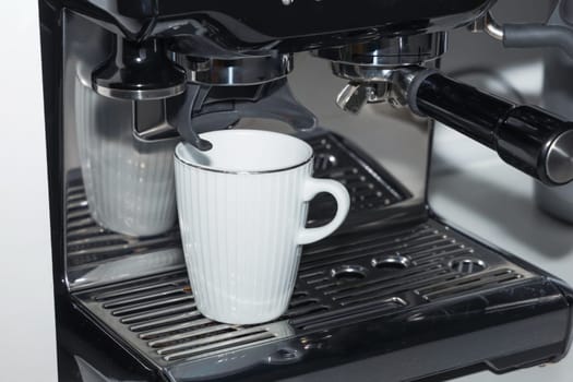 A white coffee cup is being filled with coffee from a coffee machine in a kitchen appliance