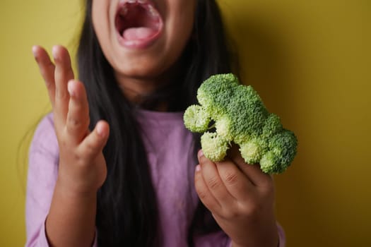 A child shows various emotions holding broccoli against a bright yellow backdrop, enjoying play