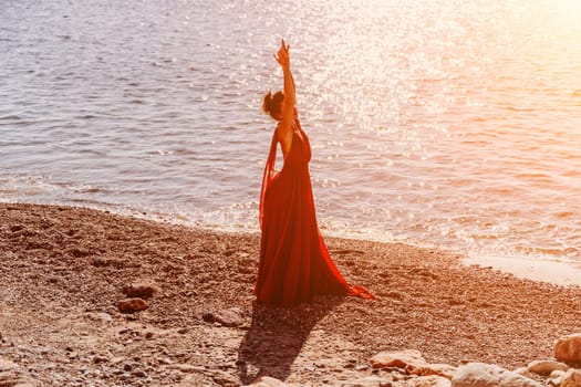 Woman red dress sea. Female dancer in a long red dress posing on a beach with rocks on sunny day. Girl on the nature on blue sky background