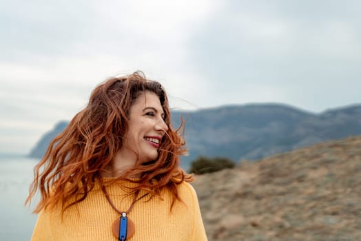 Portrait windswept hair happy woman against a backdrop of mountains and sea. Daylight illuminates the tranquil outdoor setting.