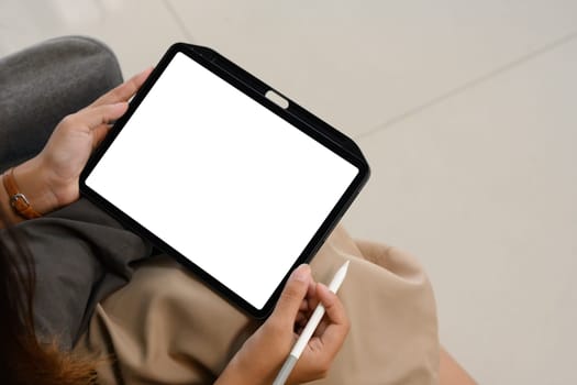 Cropped image of a woman holding digital tablet with blank desktop screen sitting on sofa.