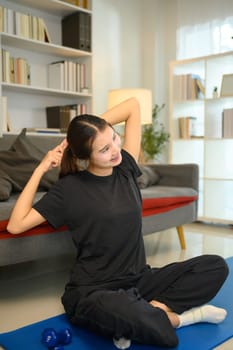 Cheerful asian young woman stretching on a yoga mat in her living room.
