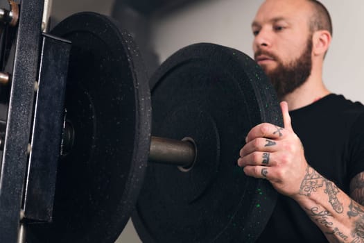 powerful sportsman in sportswear standing with black weight plate in hands putting it on press machine during workout in gym, concept of fitness and active lifestyle