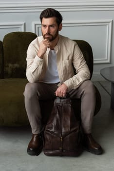 A man is comfortably seated on a sofa with a backpack resting beside him, creating a relaxed and casual atmosphere around him