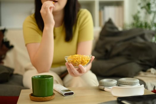 Young woman holding a bowl of cornflakes sitting in a cozy living room.