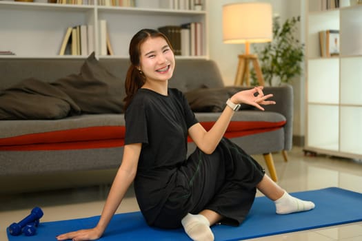 Smiling young woman practicing yoga at home. Balanced and active lifestyle concept.