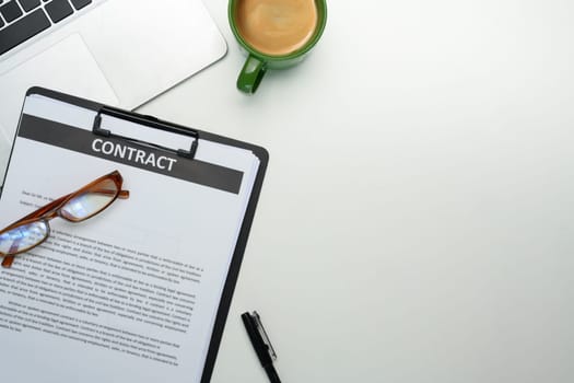 Close up of contract on clipboard, glasses, a cup of coffee and laptop on organized workspace.