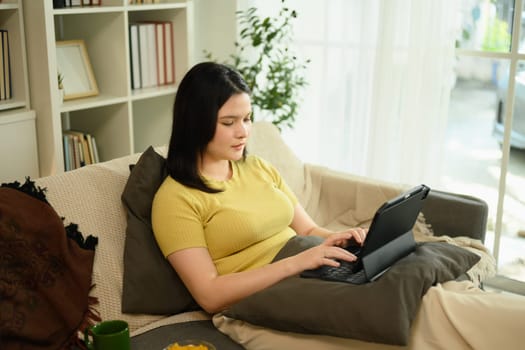 Relaxed young woman working with her digital tablet on sofa in bright living room.