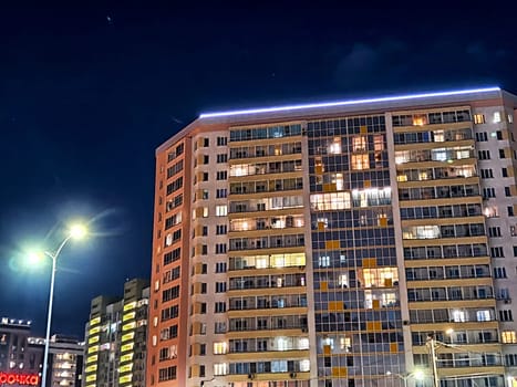 Brightly lit apartments showcase evening life in an urban building against a clear night sky.