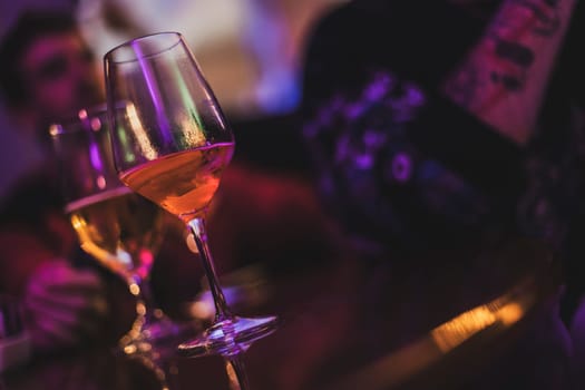 Wine glasses filled with beverages sit on a bar during an evening gathering, creating a vibrant and social atmosphere