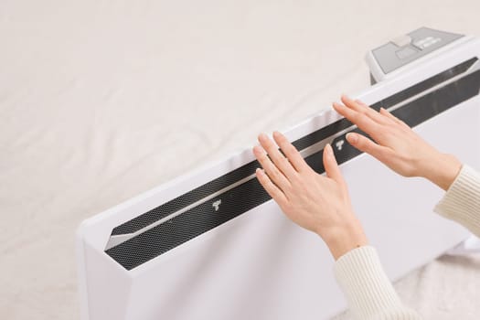 Frozen young woman with plaid warming near radiator at home, home heating concept, low temperature