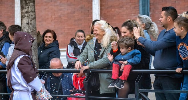 Crowd of diverse people enjoying urban festival or event, with a focus on one individual in a hooded robe