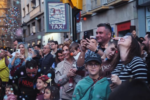 Diverse crowd enjoying a festivity in a city street, capturing moments on mobiles amongst floating bubbles.