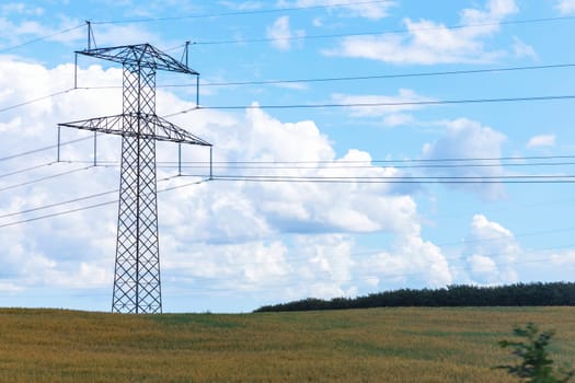 Electricity concept. High voltage power line pylons, electrical tower on a green field with blue sky. High quality photo