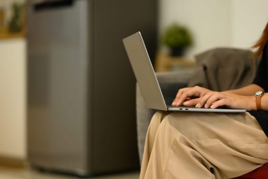 Cropped shot young woman using laptop, working remotely at home.