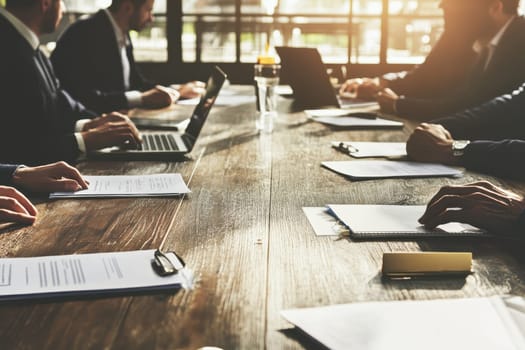 A group of professionals engaged in a corporate meeting, discussing strategies and reviewing documents at a wooden table with a laptop, emphasizing teamwork and collaboration.