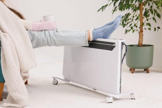Young girl in warm knitted socks warms her feet on a radiator. home heating concept, low temperature