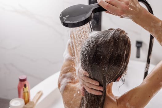 Woman washing her hair while taking shower at home, back view, hair care concept,