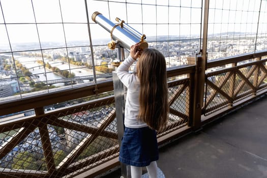 A little girl looks through a large telescope on an observation deck. High quality photo