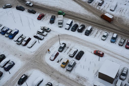 An aerial view of a vast parking lot that is completely blanketed in white snow, showcasing various cars and icy paths
