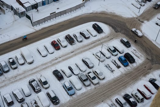 A thick layer of snow covers cars in a parking lot, forming a peaceful winter scene viewed from above