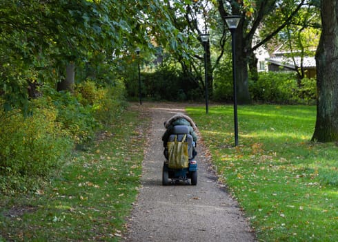 A woman in a wheelchair is driving along the road to the parks. High quality photo