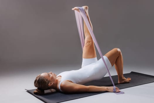 Athletic adult woman doing exercise with rubber band for fitness and pilates sitting on yoga mat.stretching exercises