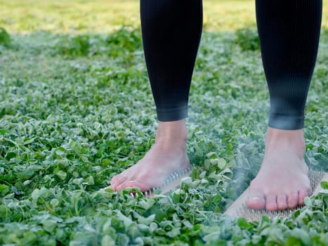 A barefoot woman stands on nails sadha board among the grass. Spiritual practice meditation in nature. Close-up