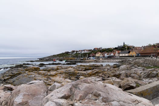 Rocky seashore and a small town in the distance in cloudy weather. Beautiful landscape. Bornholm, Denmark - December 4, 2024