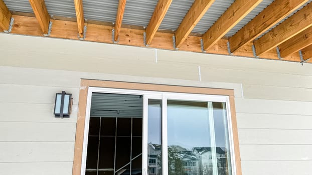 Exposed wood beam ceiling structure supporting a corrugated metal roof in a covered outdoor patio area of a newly built residential home. The design showcases natural wood framing and metal roofing components, providing durability and modern aesthetics.