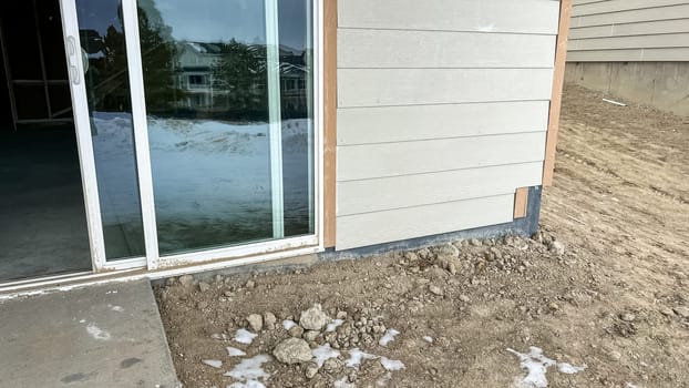 Under-construction backyard patio area featuring a sliding glass door leading to a small concrete step surrounded by dirt and snow. The unfinished landscaping and exposed ground highlight the early stages of residential development.