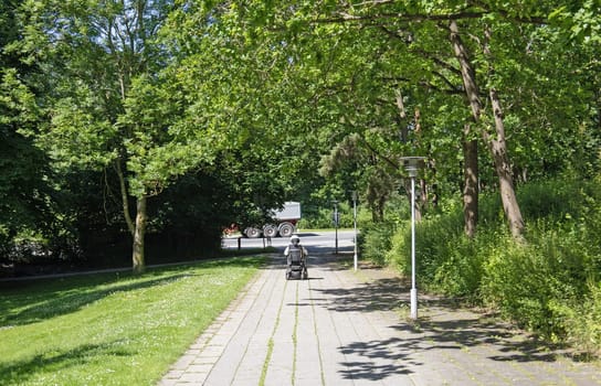 A man in a wheelchair is driving along the road to the parks. High quality photo