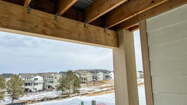 Close-up view of the exposed framing underneath a wooden deck in a newly constructed suburban home. The structure features wooden beams, metal connectors, and corrugated metal sheeting, showcasing the construction process and materials used.
