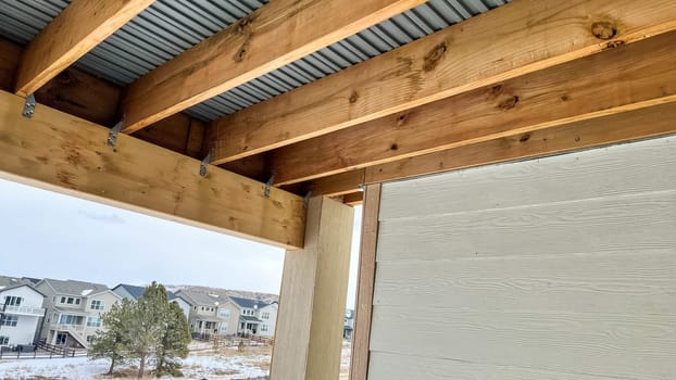 Close-up view of the exposed framing underneath a wooden deck in a newly constructed suburban home. The structure features wooden beams, metal connectors, and corrugated metal sheeting, showcasing the construction process and materials used.