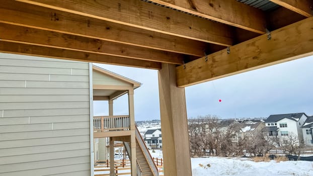 Close-up view of the exposed framing underneath a wooden deck in a newly constructed suburban home. The structure features wooden beams, metal connectors, and corrugated metal sheeting, showcasing the construction process and materials used.