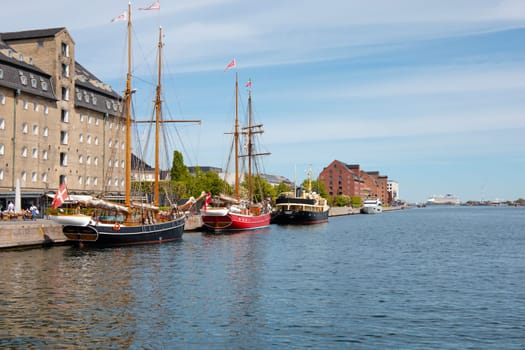 Copenhagen, Denmark - May 15, 2023. View of waterfront of Copenhagen, old houses with tiled roofs and sailing ship on a sunny summer day.