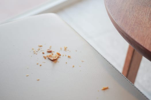 There are scattered crumbs resting on a chair surface located near a wooden table