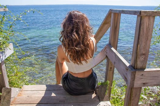 Beautiful young girl with brown hair on the seashore sits and looks at the sea. Denmerk - September 10, 2023