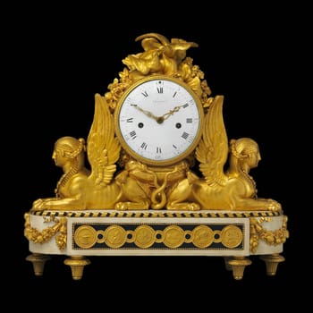 A close-up of a gilded antique clock with a perpetual calendar and moon phase display. The clock face features elegant Arabic numerals.