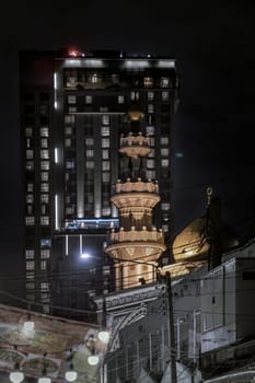 Bangkok, Thailand - Nov 22, 2024 - Architecture exterior of Mirasuddeen mosque with modern building in the background at silom road in the night. Copy space, Selective focus.