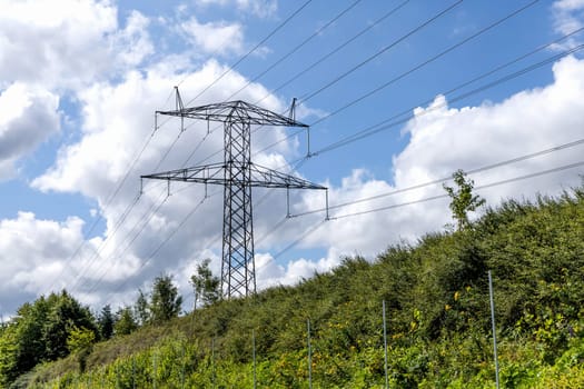Electricity concept. High voltage power line pylons, electrical tower on a green field with blue sky. High quality photo