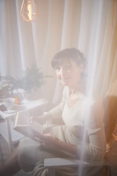 A middle-aged woman relaxes in a homely apartment, immersed in a book, surrounded by a warm, comfortable atmosphere during the evening.