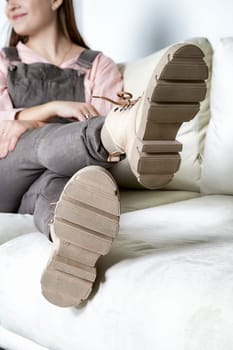 A fashionable model relaxes on a sofa, highlighting trendy shoes that complement her outfit and pose in a cozy setting.