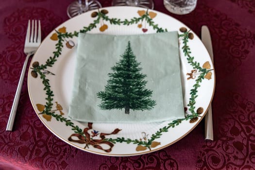 Set Christmas table with Christmas plate and crystal glasses on a red tablecloth.
