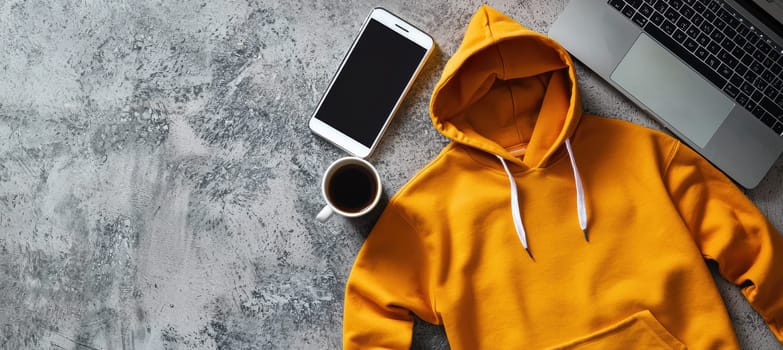 Gray hoodie, laptop, smartphone, and coffee cup arranged on a textured surface. ideal for showcasing casual work from home or remote work style. emphasizes comfort and modern lifestyle trends in professional settings.