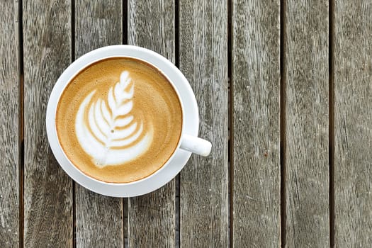 White cup of coffee with pattern on top of foam, against background of wooden table, copy space, top view