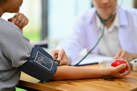 Doctor measuring arterial blood pressure of elderly lady in hospital. Elderly healthcare and hypertension concept.